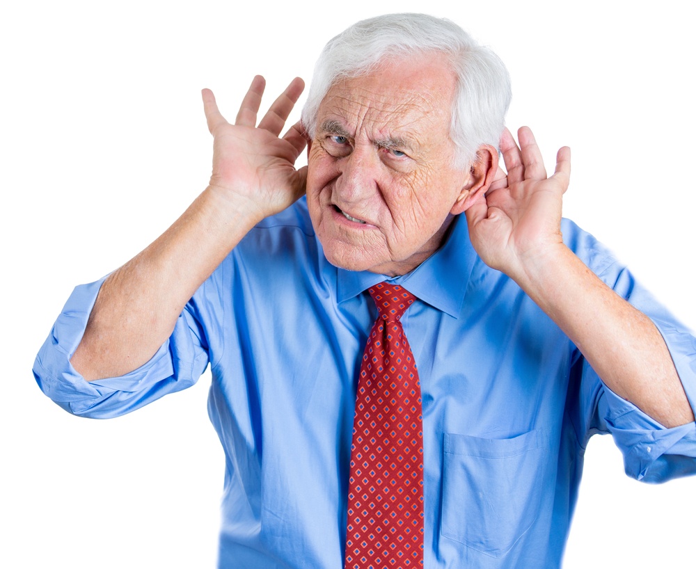 A close-up portrait of an elderly executive looking unhappy and annoyed,having trouble hearing his opponent, during unpleasant conversation, isolated on a white background . Hearing aid..jpeg